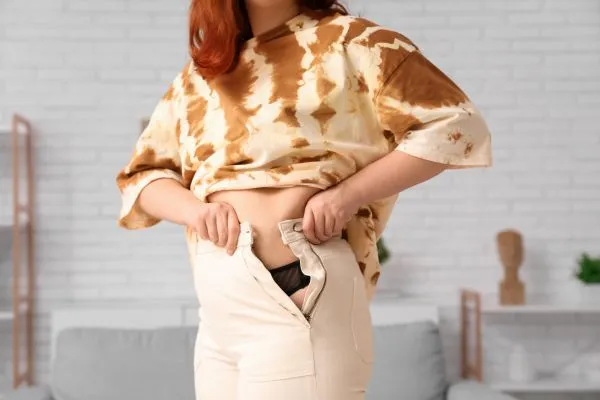 Image of woman trying to do her trousers up after pregnancy weight gain West Malling