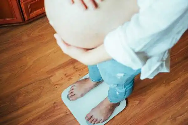 Image of woman weighing herself and experiencing weight gain through pregnancy West Malling